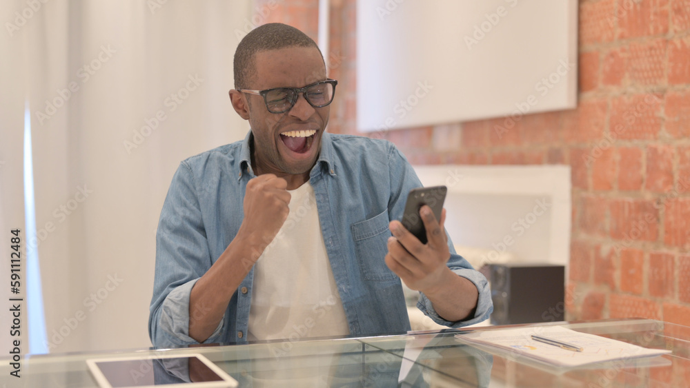 African Man Celebrating Success on Smartphone African Man Celebrating Success on Smartphone