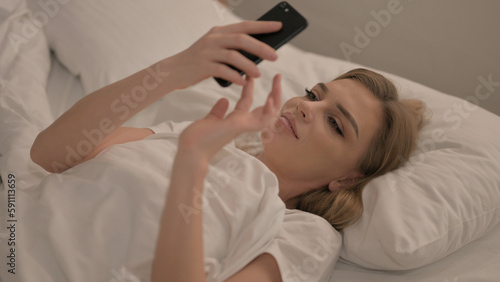 Young Woman using Smartphone while Lying in Bed