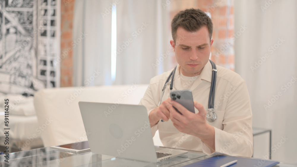 Male Doctor Using Laptop and Smartphone in Clinic Male Doctor Using Laptop and Smartphone in Clinic