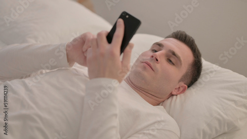 Young Man using Smartphone while Lying in Bed