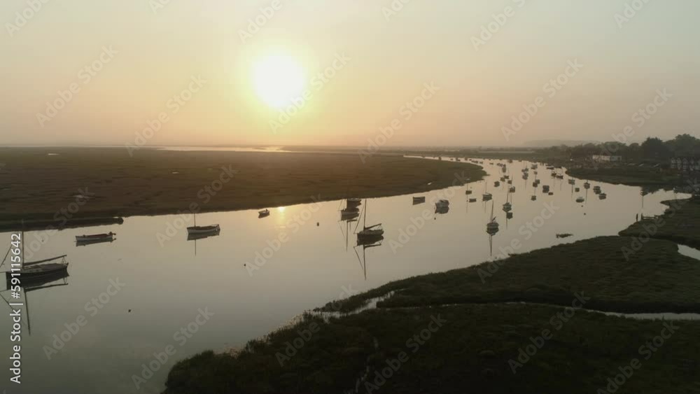 Establishing Aerial Drone Shot Flying Over Burnham Overy Staithe Creek with Sailing Boats and Salt Marsh into the Sun at Sunrise on Misty Morning in North Norfolk UK East Coast