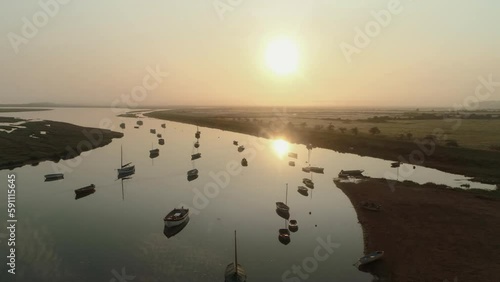 Pullback Aerial Drone Shot of Sailing Boats in Creek at Sunrise into the Sun on Misty Morning at Burnham Overy Staithe North Norfolk UK East Coast photo