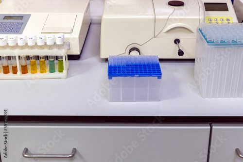 laboratory table with multi-colored reagent vials in the stand, disposable plastic test tubes and measurement machines photo