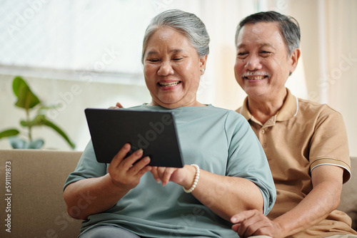 Joyful senior couple watching episode of show on tablet computer