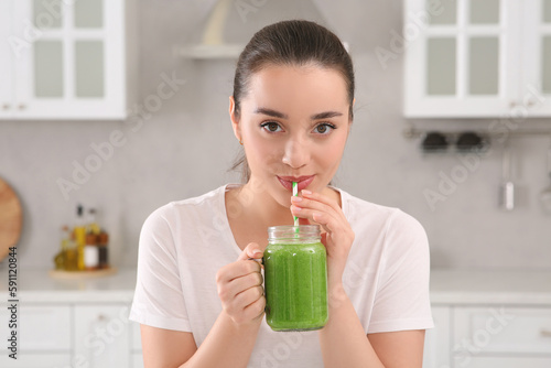 Beautiful young woman drinking delicious smoothie in kitchen