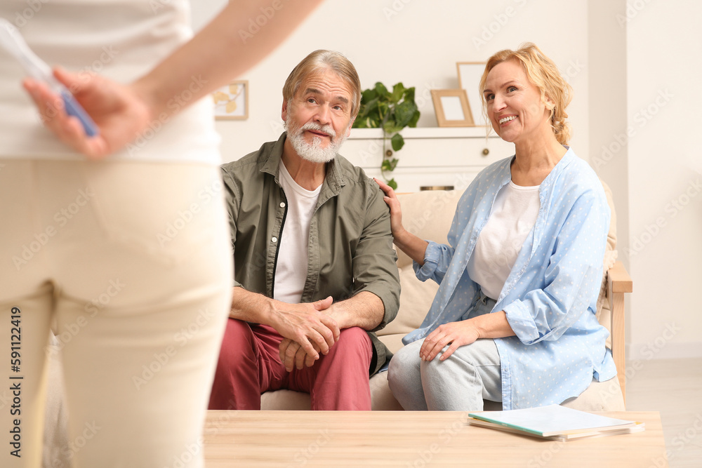 Obraz premium Woman holding pregnancy test behind her back near parents indoors. Grandparents' reaction to future grandson