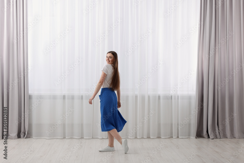 Woman standing near window with stylish curtains at home