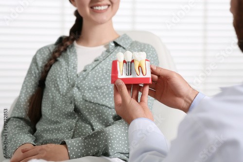 Doctor with educational model of dental implant consulting patient in clinic, closeup