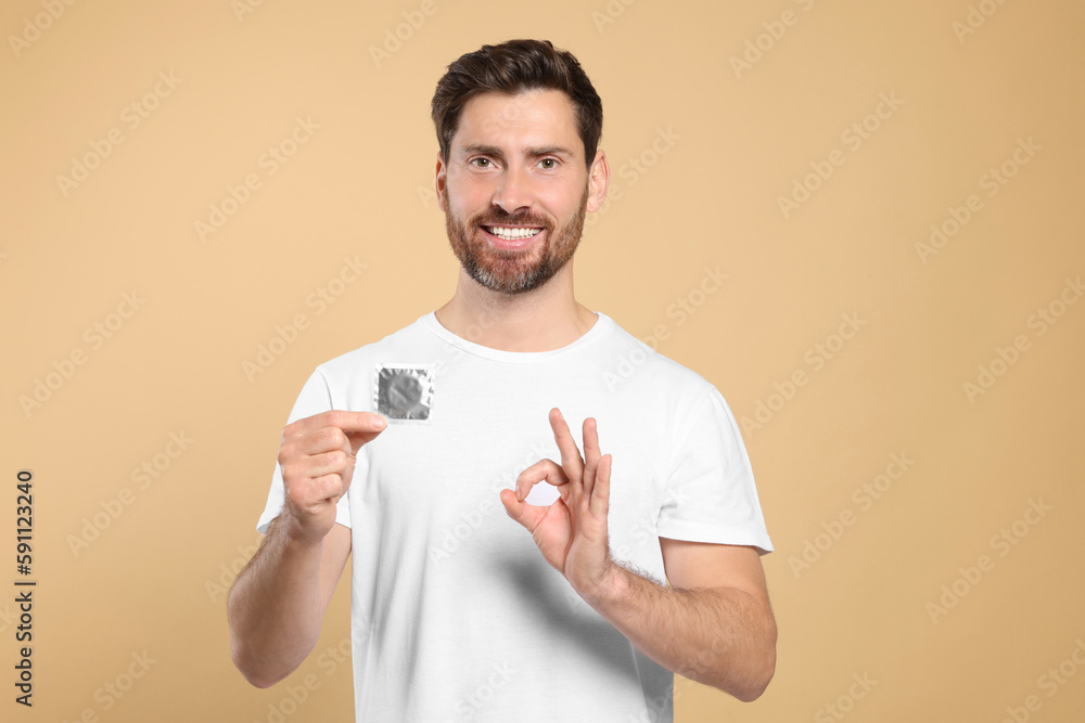 Man with condom showing ok gesture on beige background. Safe sex Man with condom showing ok gesture on beige background. Safe sex