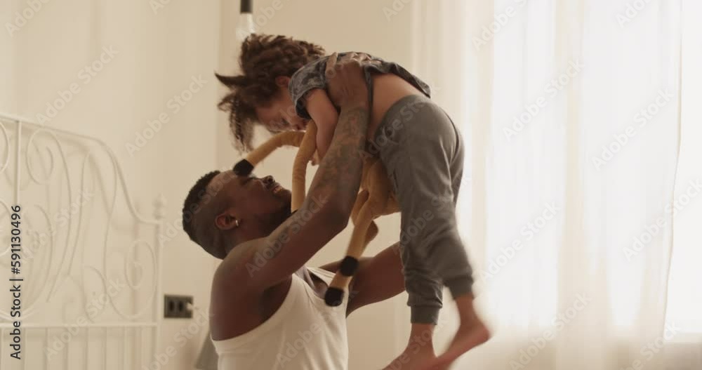 Delighted African American man playing with cute daughter on bed Delighted African American man playing with cute daughter on bed