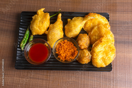 Indian Tea time snacks in group includes Veg Samosa, Kachori/kachaudi, aloo bonda, khaman dhokla, bread, onion,chilli and moong pakora/pakoda/bhaji/bhajji/Bhajiya/bajji with sauces, selective focus photo