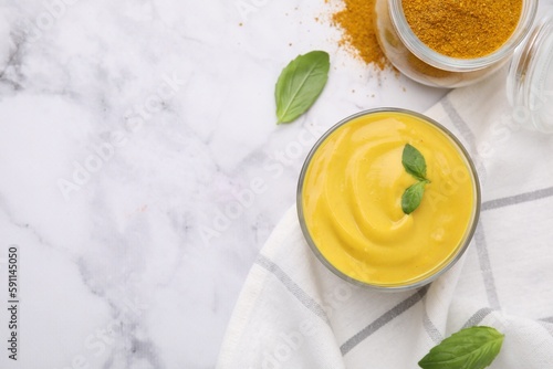 Tasty curry sauce, powder and basil leaves on white marble table, flat lay. Space for text