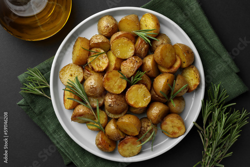 Delicious baked potatoes with rosemary and oil on black table, top view