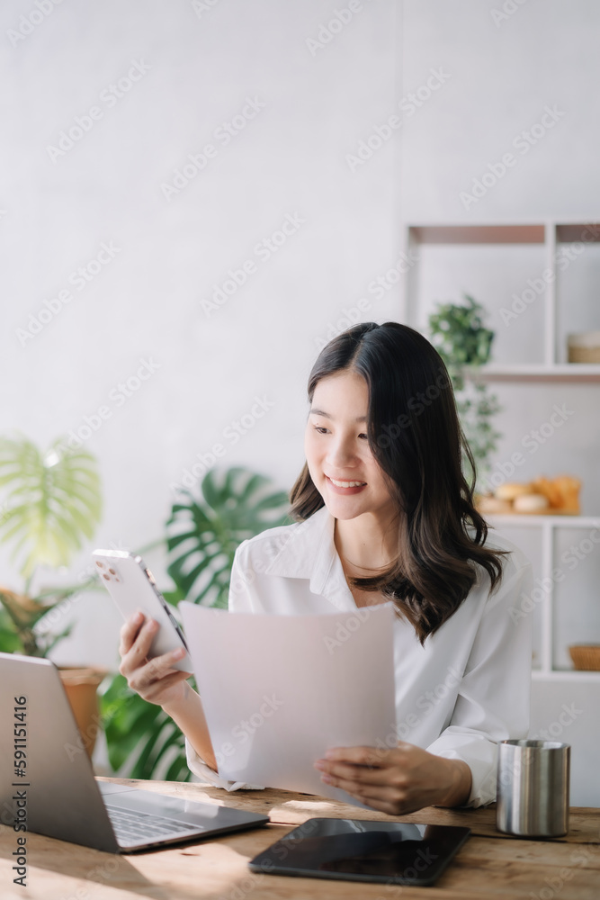 Asian businesswoman talking mobile phone and working on laptop and papers on table in her office. Asian businesswoman talking mobile phone and working on laptop and papers on table in her office.