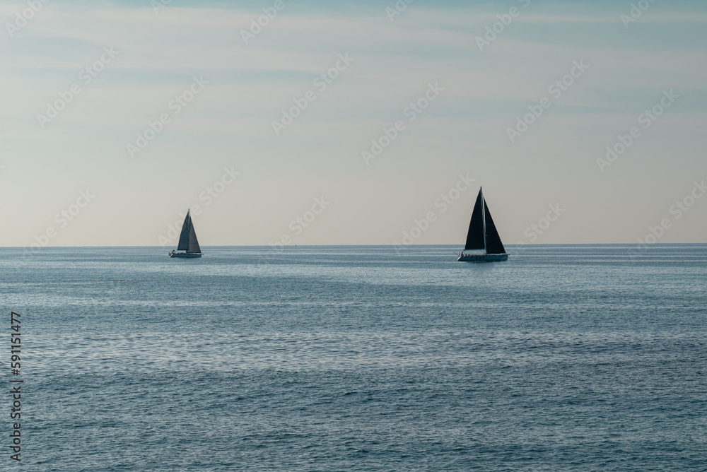 A beautiful composition of two sail boats sailing on a blue Tyrrhenian Sea near Tropea, popular travel destination. A great summer holiday tourist attraction, recreational activity in Italy.