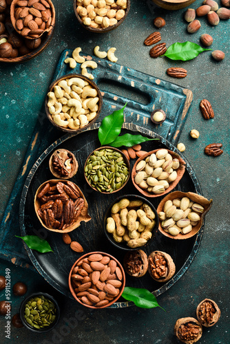 Peanuts, walnuts, almonds, hazelnuts and cashews mixed together in wooden bowls. Top view. On a dark background.