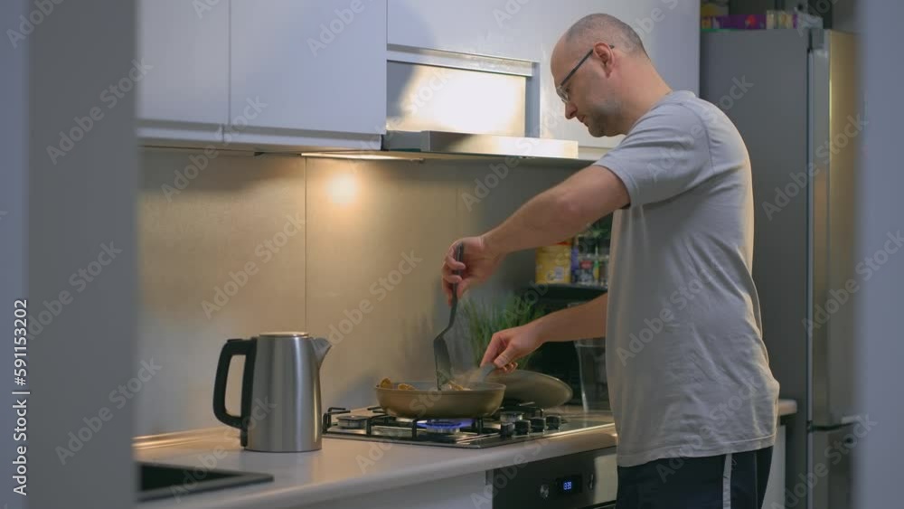Man cooking fried chicken meat in pan in kitchen for his lovely wife. Hobby, preparing food home, modern interior, cookery concept Man cooking fried chicken meat in pan in kitchen for his lovely wife. Hobby, preparing food home, modern interior, cookery concept