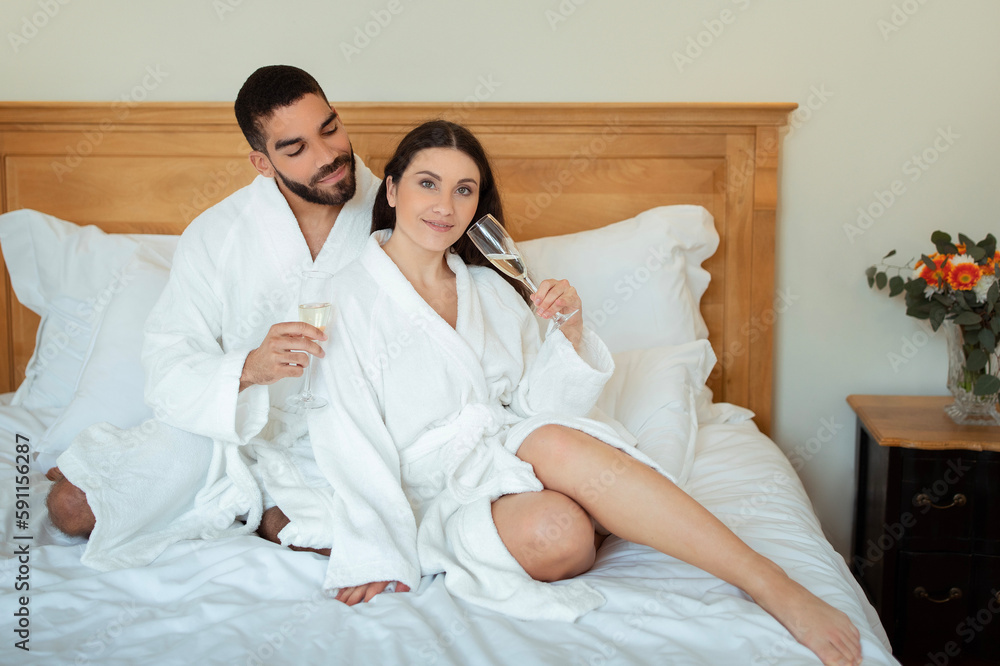 Fototapeta premium Couple Drinking Champagne Sitting On Bed Enjoying Taste In Hotel