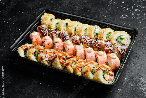 Big set of Sushi rolls with cheese and fish and caviar, Japanese food. Delivery. Disposable tableware. On a black stone background.