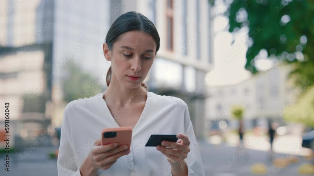 Caucasian Girl Business Woman Customer Buyer Stands in City, Makes Purchase Online Using Mobile Phone Smartphone and Bank Card Enters Number for Transaction Order Pays in Shopping App Caucasian Girl Business Woman Customer Buyer Stands in City, Makes Purchase Online Using Mobile Phone Smartphone and Bank Card Enters Number for Transaction Order Pays in Shopping App