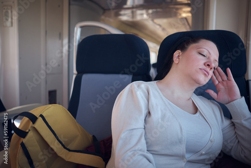 Woman sleeping in a train seat while travelling. © astrosystem