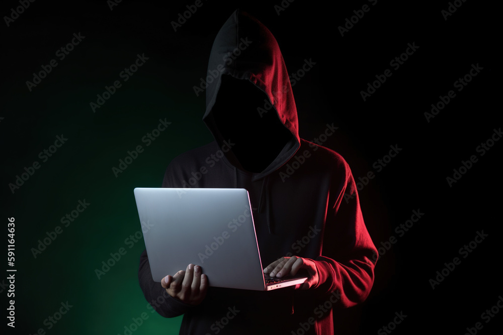 a hacker in a hoodie using a laptop computer isolated on dark background with neon light. Created with Generative AI Technology a hacker in a hoodie using a laptop computer isolated on dark background with neon light. Created with Generative AI Technology