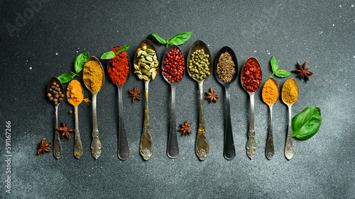 Fototapeta Naklejka Na Ścianę i Meble -  A set of colored spices in metal spoons. On a black slate background. Top view.
