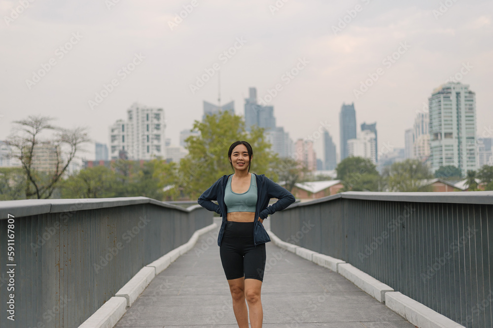 Asian happy woman exercise in park on morning. Healthy confident female wearing sportswear standing and smiling in outdoors. wellness lifestyle, outside activities.