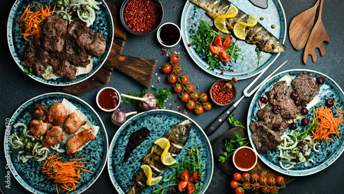 Fototapeta Naklejka Na Ścianę i Meble -  A set of meat dishes: shish kebab, kebab, steak, fish. On a black background. Top view. Free space for text.