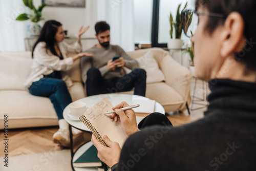 Woman psychologist writing down notes during therapy session with married couple