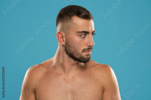 Handsome adult shirtless man withbeard and serious, looking aside confident standing against studio background