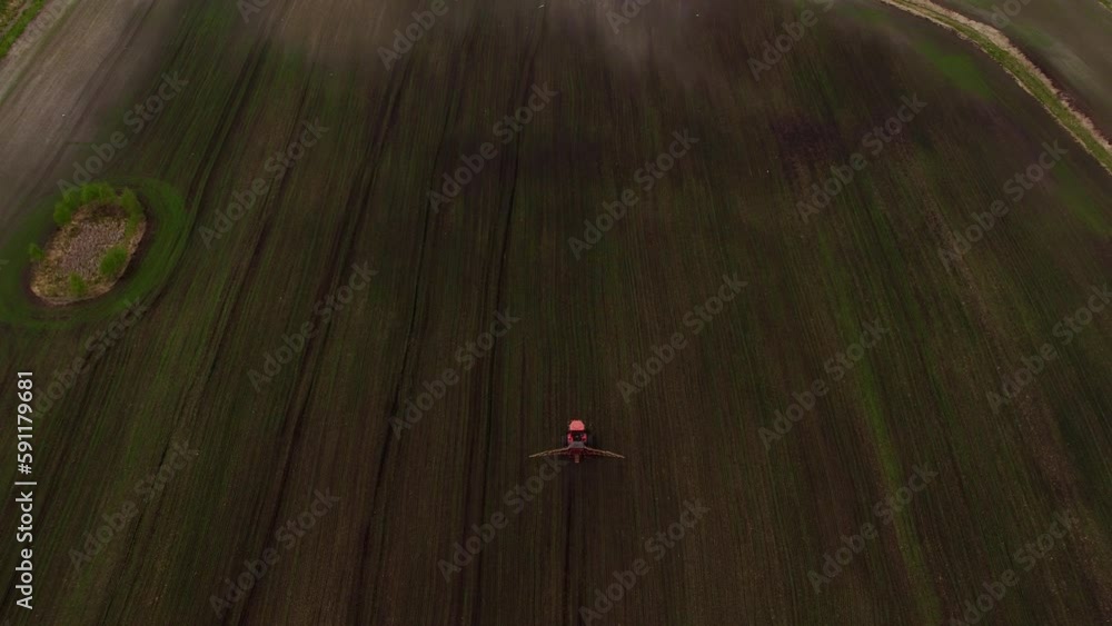 Top view frome drone of a red tractor plows the ground in the field for planting countryside, the camera follows moving forward Top view frome drone of a red tractor plows the ground in the field for planting countryside, the camera follows moving forward