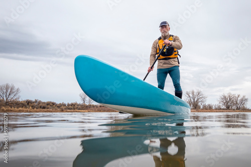 solo senior male paddling a stand up paddleboard on a lake in early spring, frog Fototapet