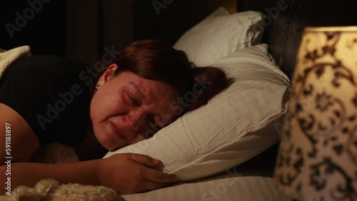 Distressed woman lie on pillow in bed and cry bitterly in dark bedroom. Splash out emotions, sob with tears. Emotional breakdown, stress, sufferings. Depression, night hysterics before sleep.