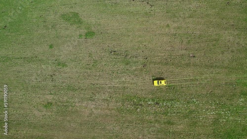 Top view of a yellow retro car ride through the green spring meadow full of grass and white flowers, tracking camera