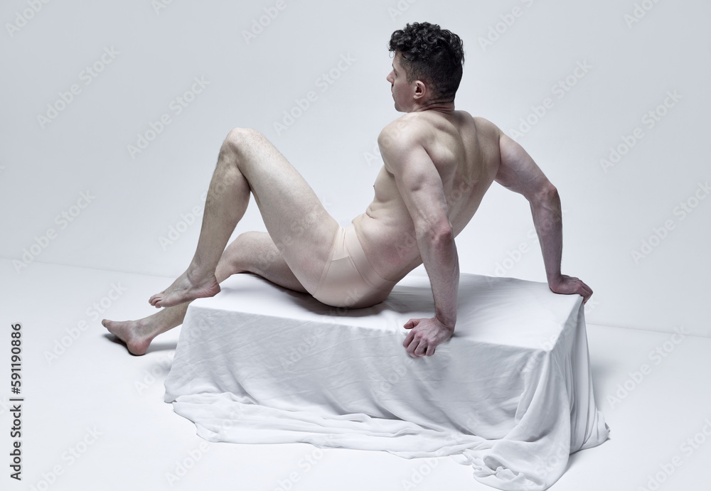 Obraz premium Natural beauty. Portrait of muscular man sitting, posing in statue pose shirtless against grey studio background. Like antique sculpture. Male body aesthetics, men's beauty, inspiration, art concept