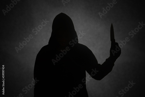 Mysterious man wearing black hoodie holding a knife to stab someone. Crimes and criminality concept photo
