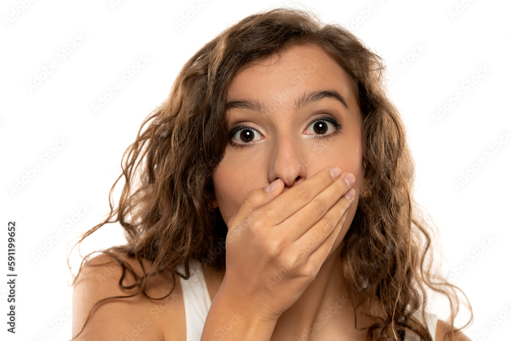 young beautiful shocked girl covering her mouth with her hands on a white studio background young beautiful shocked girl covering her mouth with her hands on a white studio background