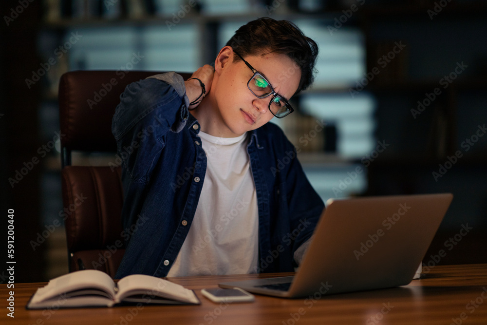 Young guy employee working on laptop, touching neck Young guy employee working on laptop, touching neck