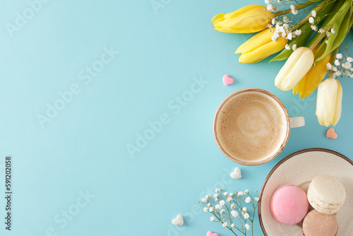 Mother's Day atmosphere concept. Top view photo of cup of coffee plate with macaroons small hearts colorful tulips and gypsophila flowers on pastel blue background with blank space