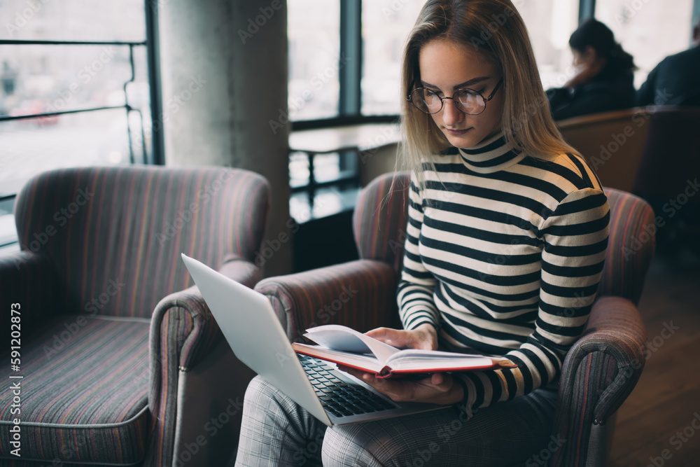 Focused woman looking for notes in notebook while working on computer Focused woman looking for notes in notebook while working on computer