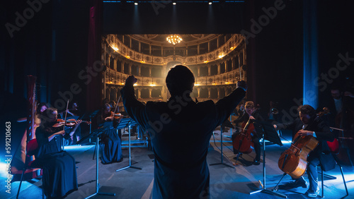 Back View Cinematic shot of Conductor Directing Symphony Orchestra with Performers Playing Violins, Cello and Trumpet on Classic Theatre with Curtain Stage During Music Concert