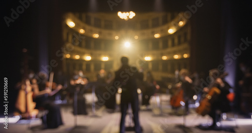 Unfocused Photo for Background Usage: Back View of Professional Conductor Directing Symphony Orchestra with Performers on Classic Theatre with Curtain Stage During Music Concert. Out of Focus