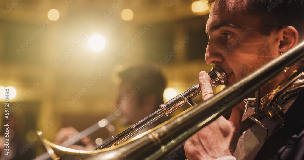 Obraz premium Cinematic Closeup of a Male Trumpet Player Reading a Music Sheet and Playing his Instrument. Professional Musician Rehearsing Before the Start of a Big Jazz Show with his Symphony Orchestra on Stage