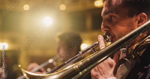 Cinematic Closeup of a Male Trumpet Player Reading a Music Sheet and Playing his Instrument. Professional Musician Rehearsing Before the Start of a Big Jazz Show with his Symphony Orchestra on Stage photo