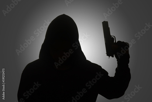 Mysterious man wearing black hoodie holding a pistol, shooting with a gun. Silhouette and dark concept image