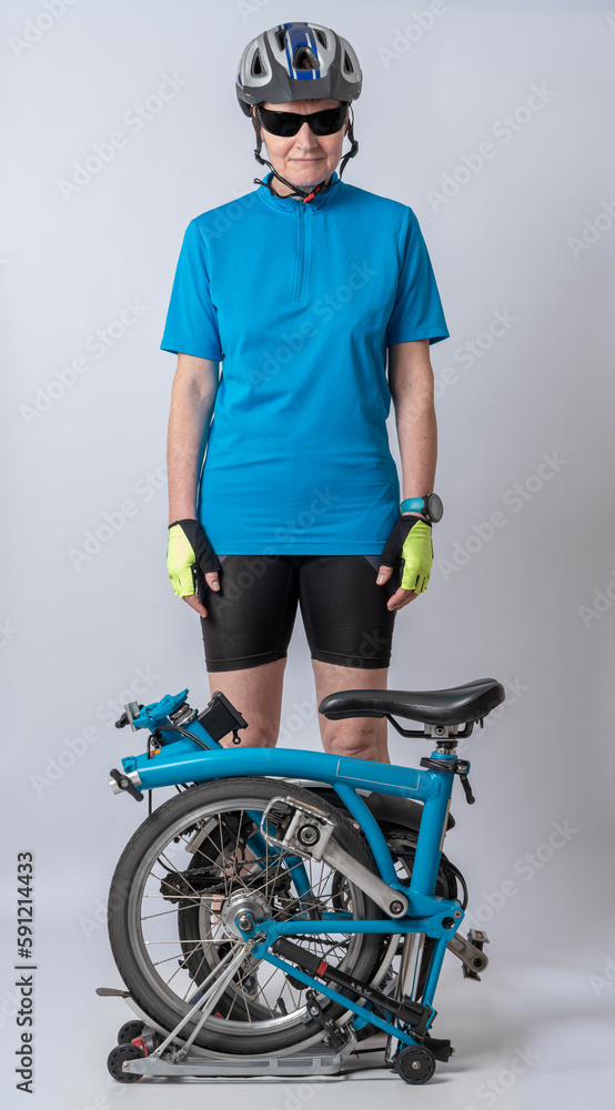 Fototapeta premium Gennevilliers, France - 04 10 2023: Studio shot detail of a woman dressed in a blue polo shirt, black shorts and a bicycle helmet, poses next to her blue folding bicycle.