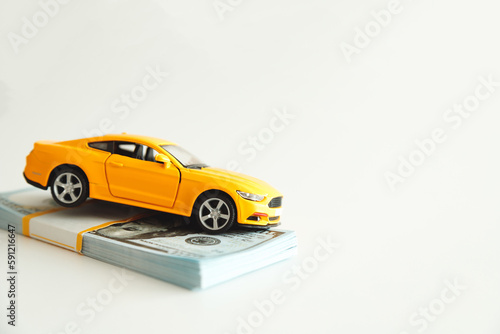 Toy Car Hanging on a Stack of Money on a White Background. Concept Car Expenses  loan payment