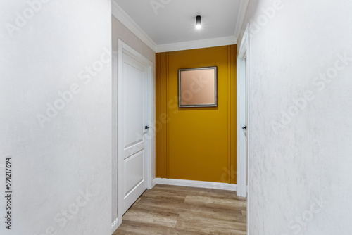 White door to the room at the end of a long corridor with a yellow wall and a painting