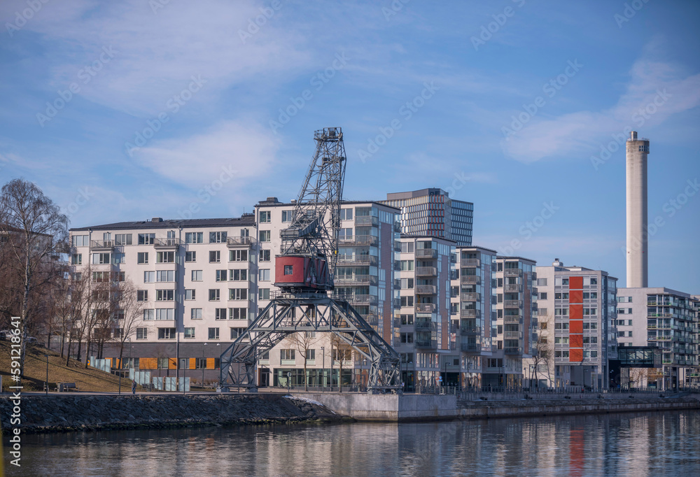 Waterfront apartment house, harbor crane and boats at a pier in the bay Hammarby sjö, a sunny spring day in Stockholm